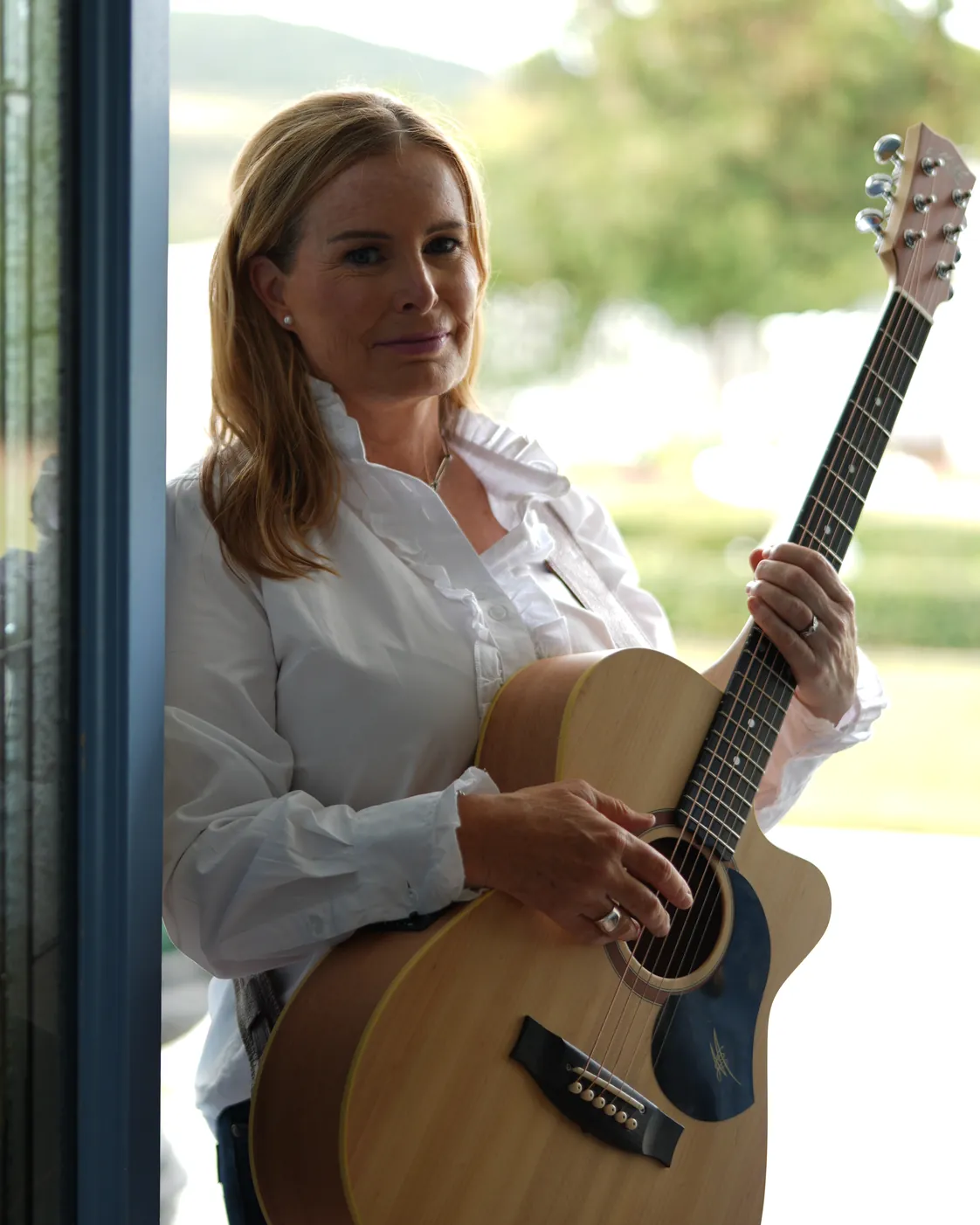 Brooke Seabrook holding her acoustic guitar by a glass door